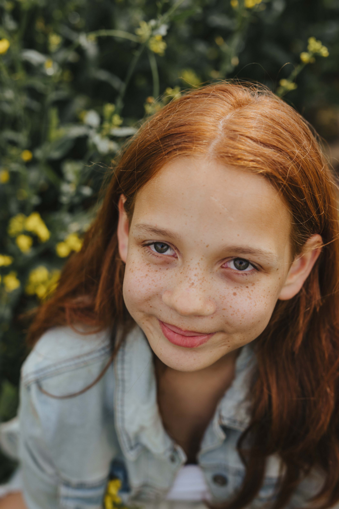 Teenager im Rapsfeld. Fotoshooting. Rote Haare. Grinsen eines Kindes. Sommersprossen und rote Haare