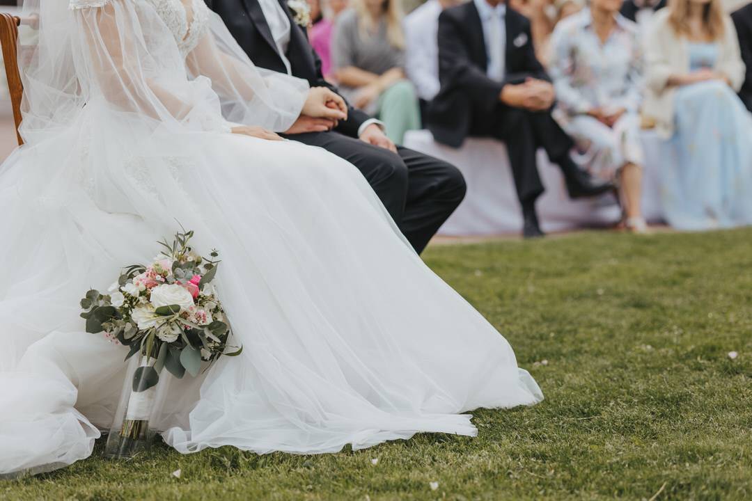 Detailbild von sitzendem Brautpaar bei freier Trauung mit Fokus auf den Brautstrauß